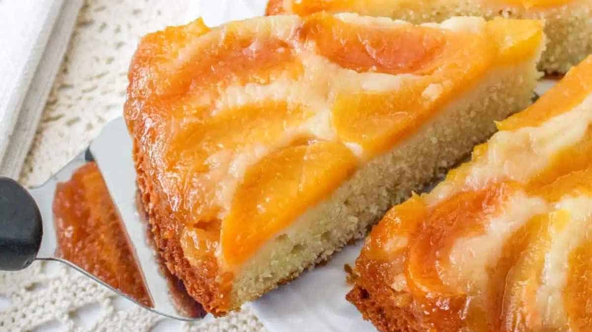 A slice of peach upside-down cake on a white plate with a cake server.