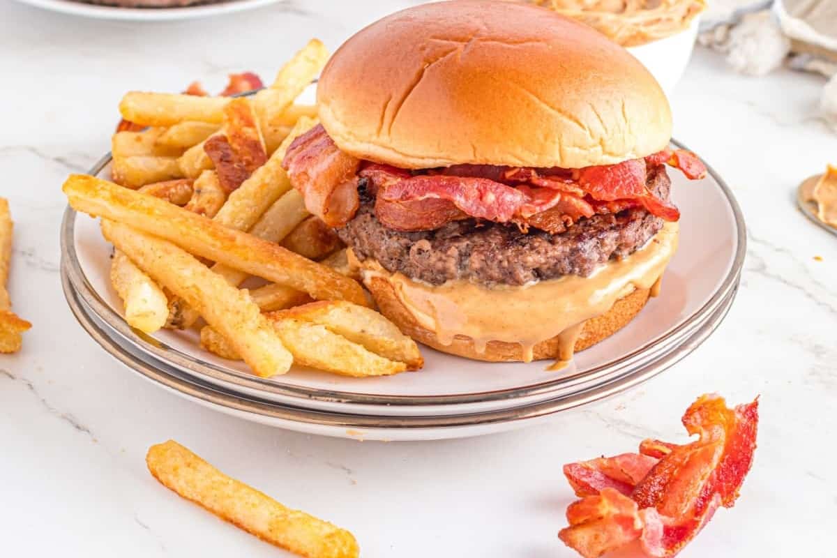 A cheeseburger with bacon on a plate accompanied by a side of french fries.