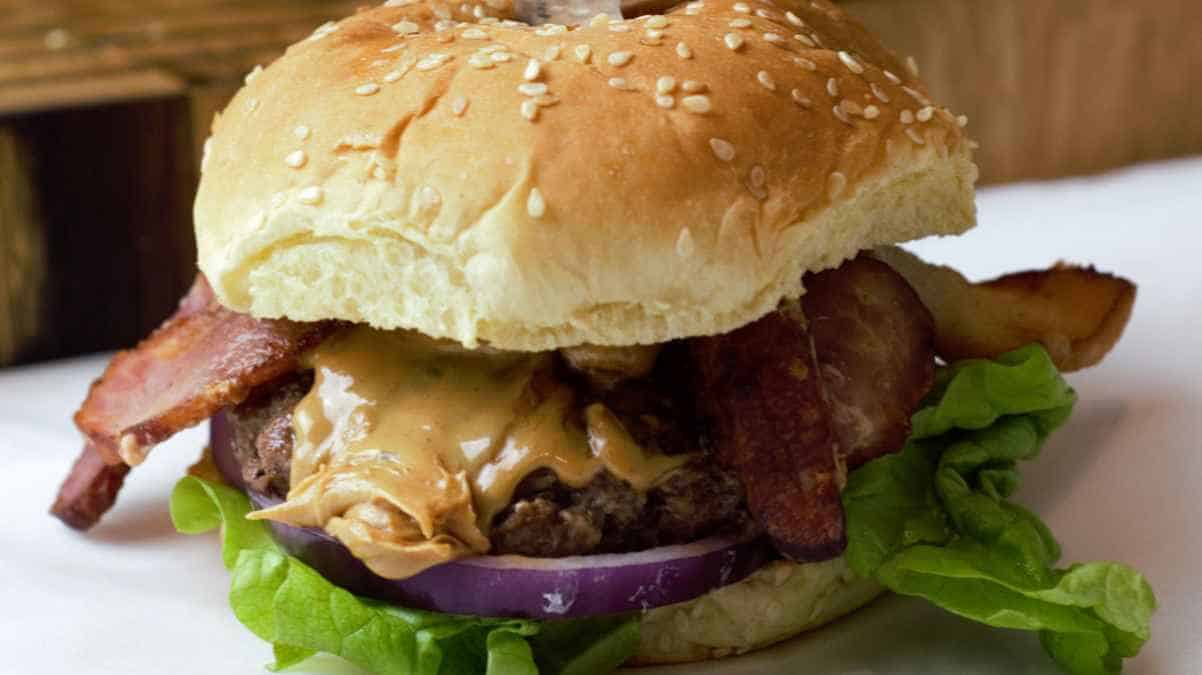 A cheeseburger with bacon, lettuce, and onion on a sesame seed bun.