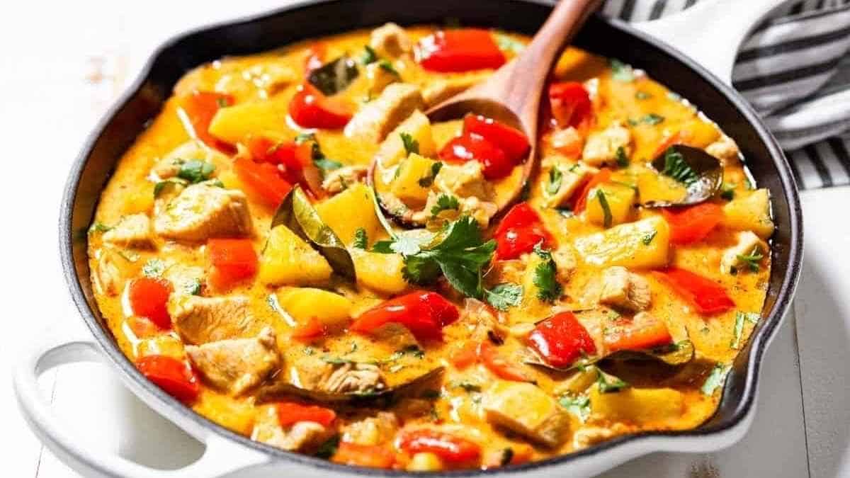 Thai chicken curry in a skillet with vegetables and a wooden spoon.