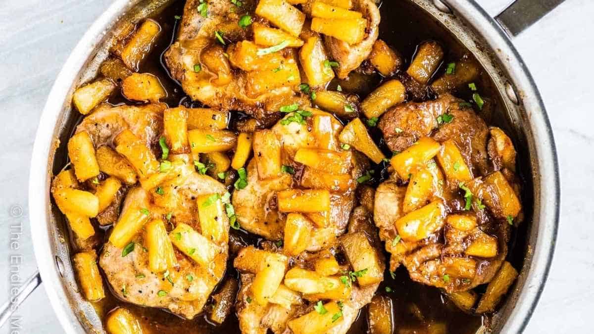 Pork chops in a skillet with apples and potatoes.