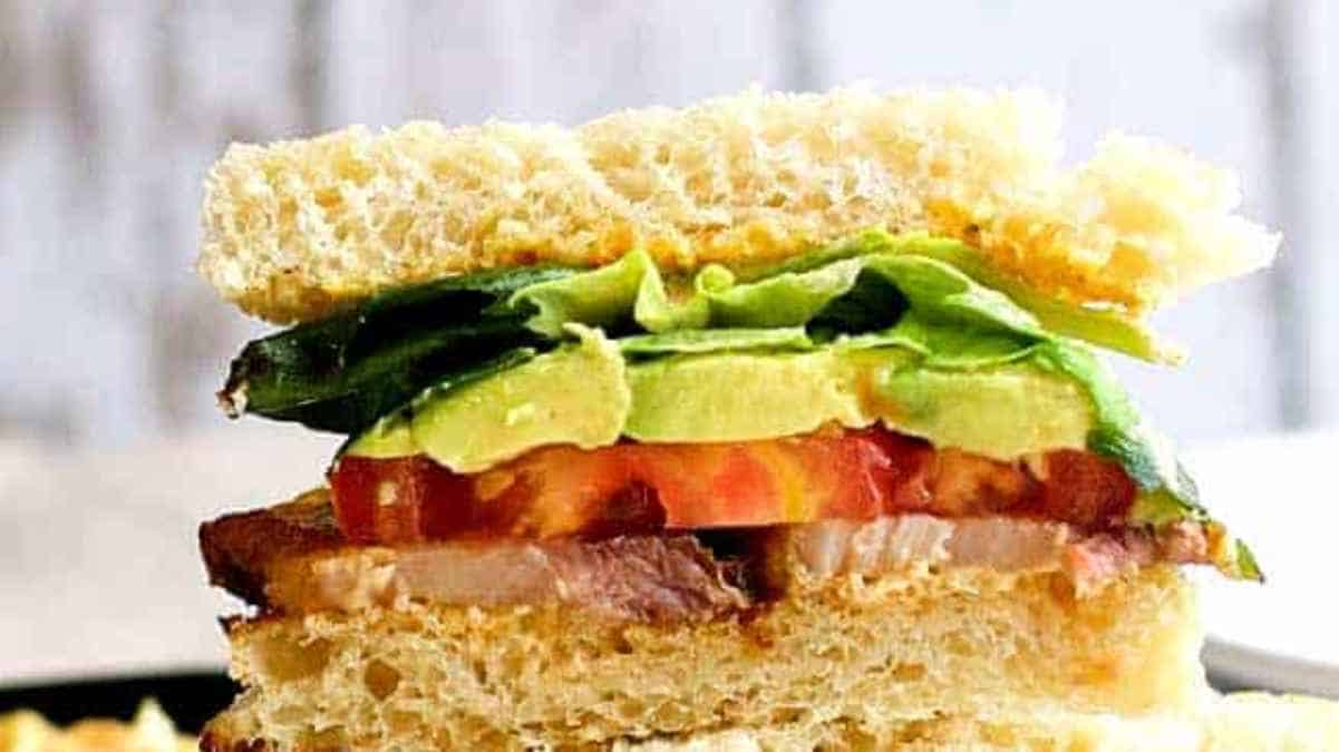 A close-up of a sandwich with avocado, bacon, lettuce, and tomato.