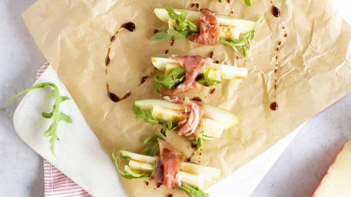 Pear and prosciutto salad with arugula and a balsamic glaze on parchment paper.
