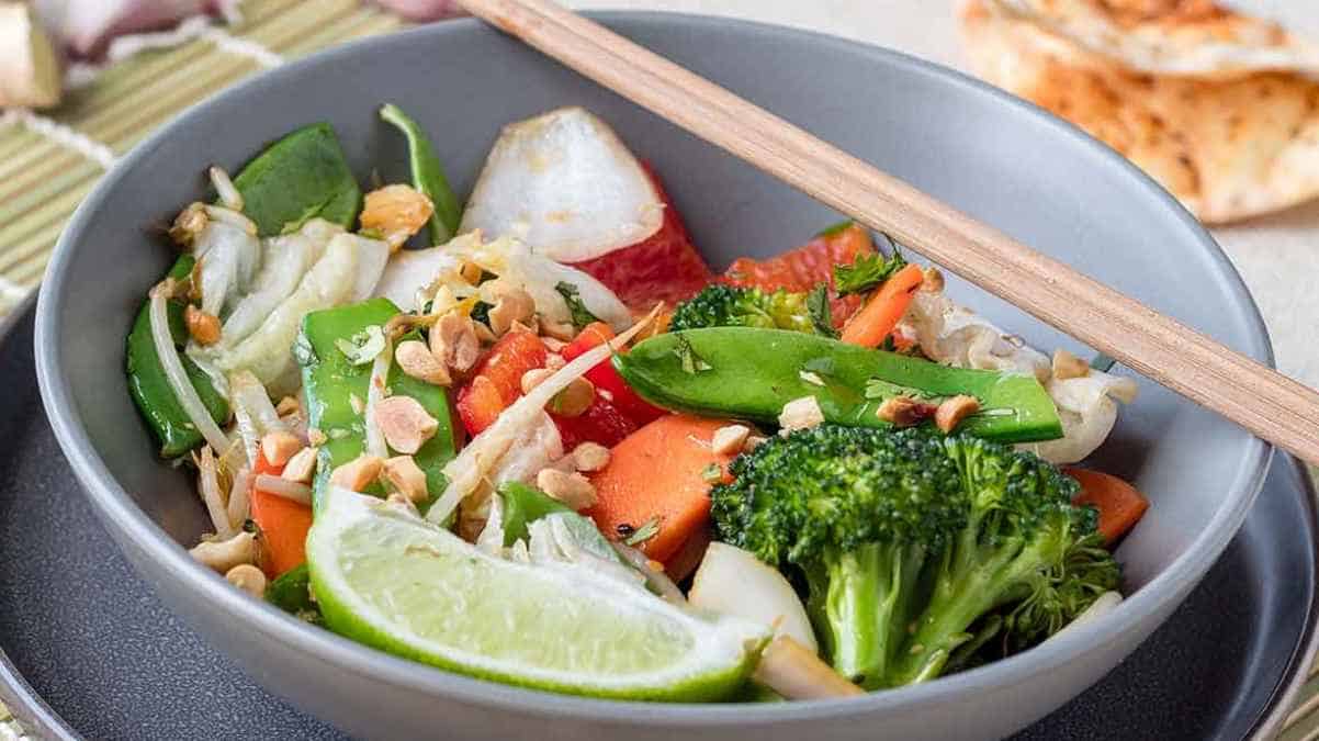 A bowl of asian-inspired vegetable stir-fry with lime and chopsticks.