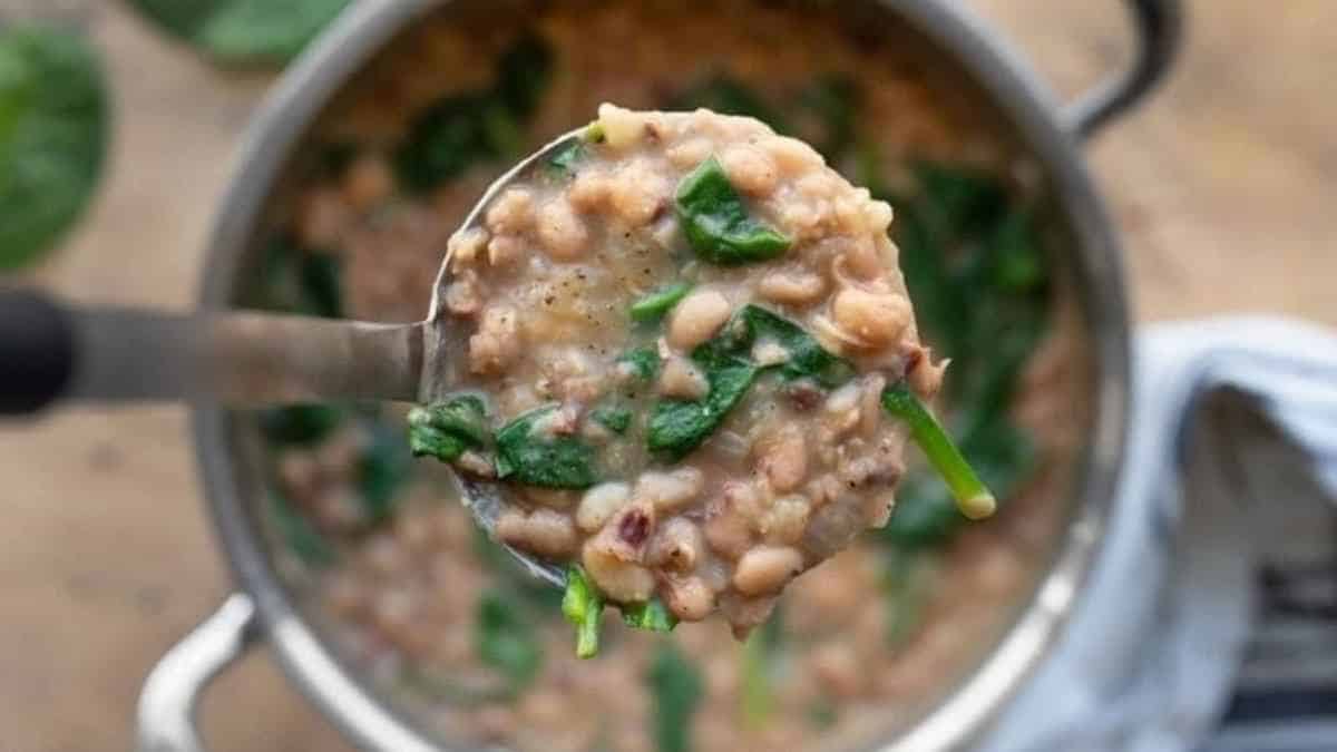 A ladle of hearty bean and spinach soup held above a pot.