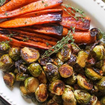 A plate of roasted carrots and brussels sprouts garnished with thyme.