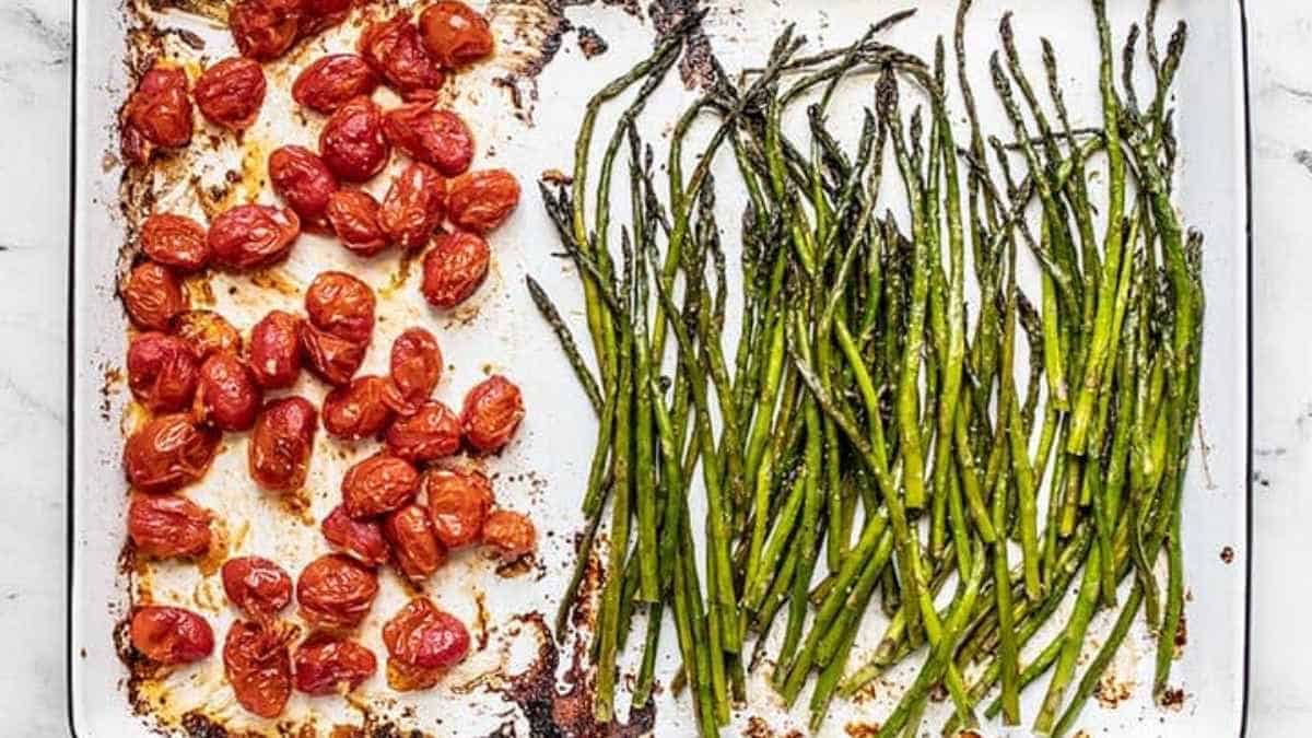 Roasted cherry tomatoes and asparagus on a baking sheet.