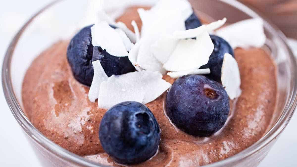 A bowl of chocolate mousse topped with fresh blueberries and coconut shavings.