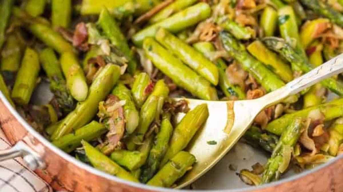 Sautéed green asparagus in a pan with seasoning.