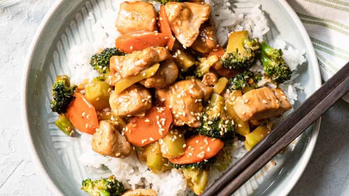 Stir-fried chicken and vegetables served over rice and garnished with sesame seeds.