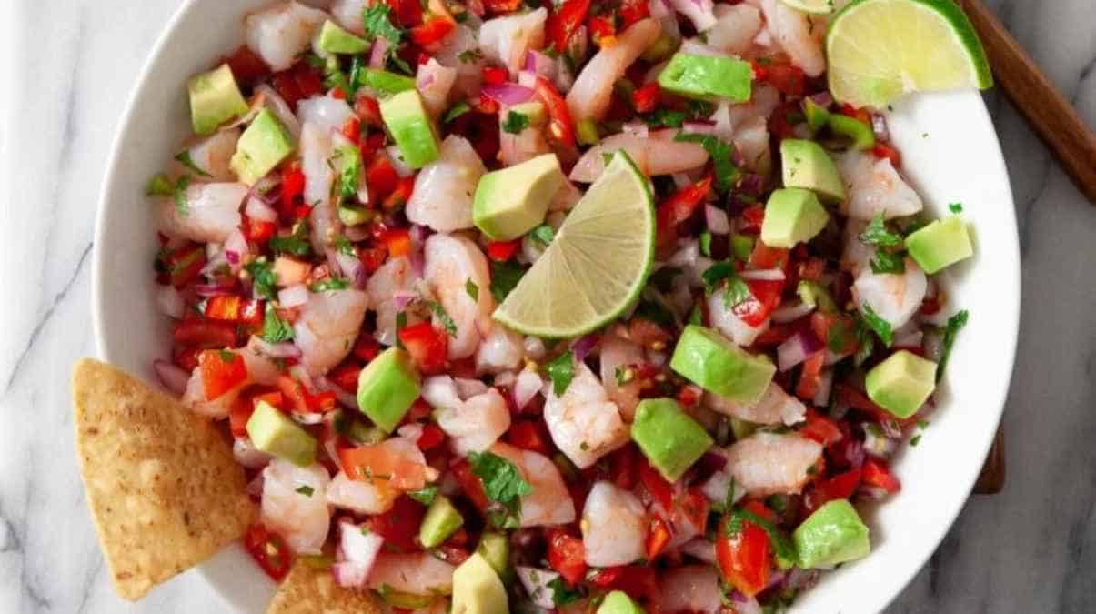 A bowl of fresh ceviche garnished with lime wedges and served with tortilla chips.