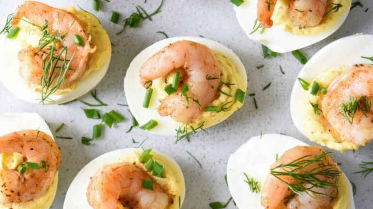 Deviled eggs topped with shrimp and garnished with dill and chives.