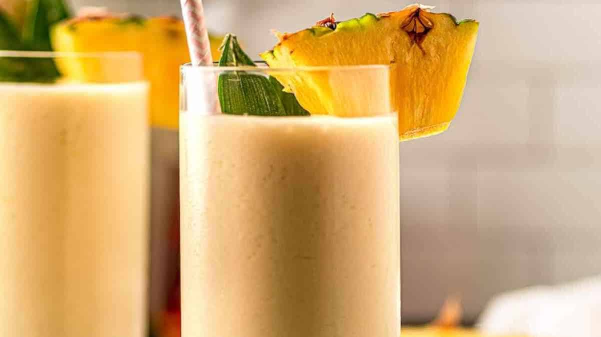 Two glasses of pineapple smoothie garnished with pineapple slices.