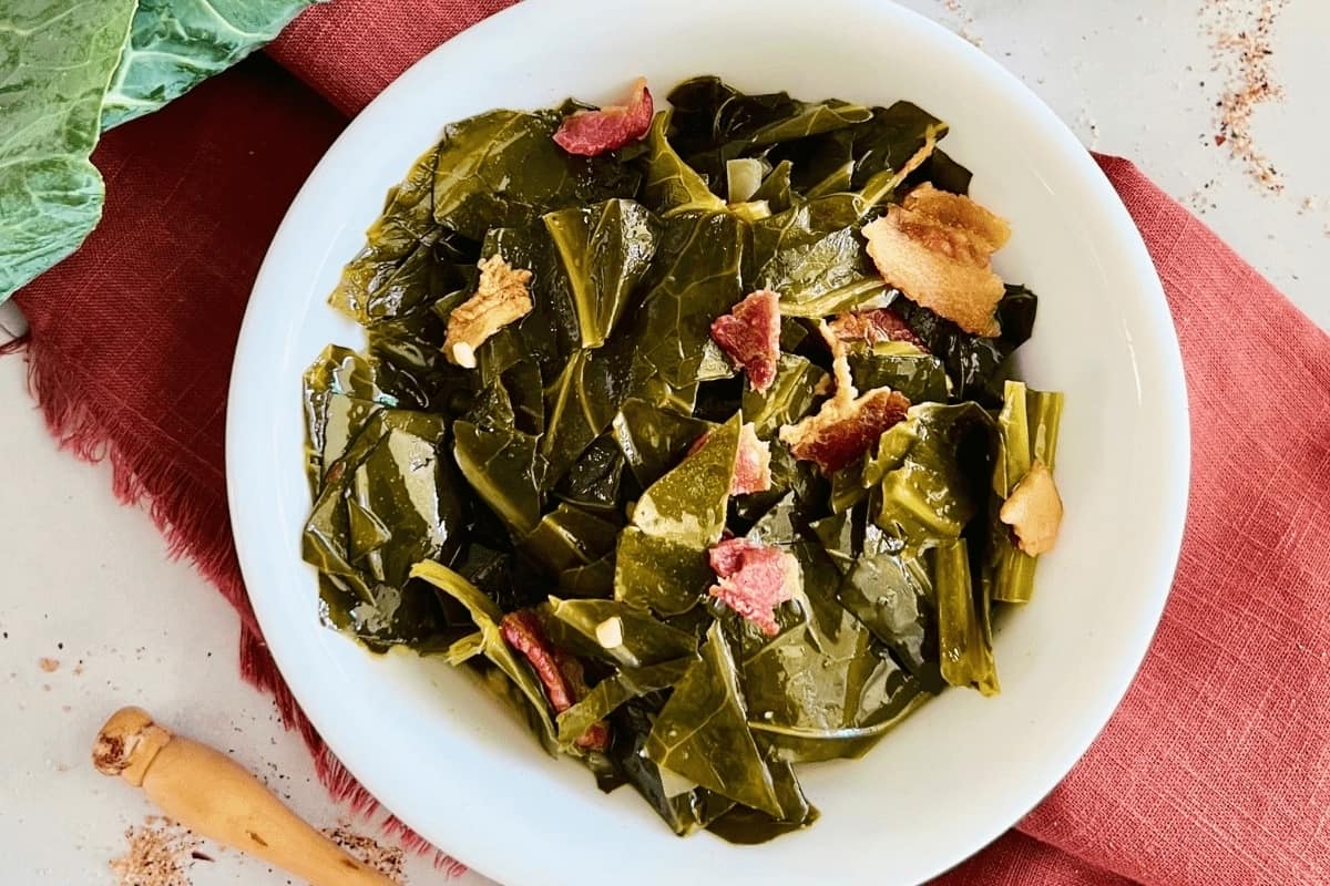A bowl of collard greens with pieces of bacon, served on a table.