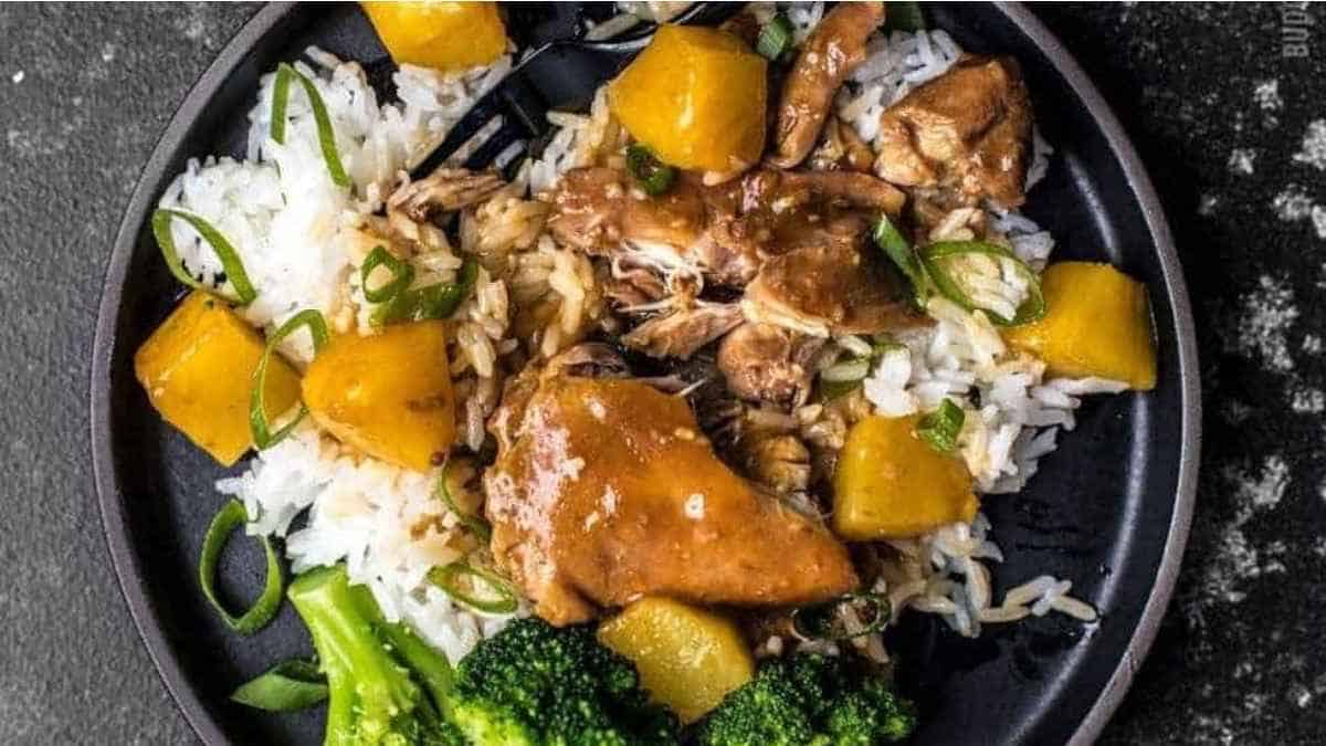 A black plate with chicken, broccoli and pineapple on it.