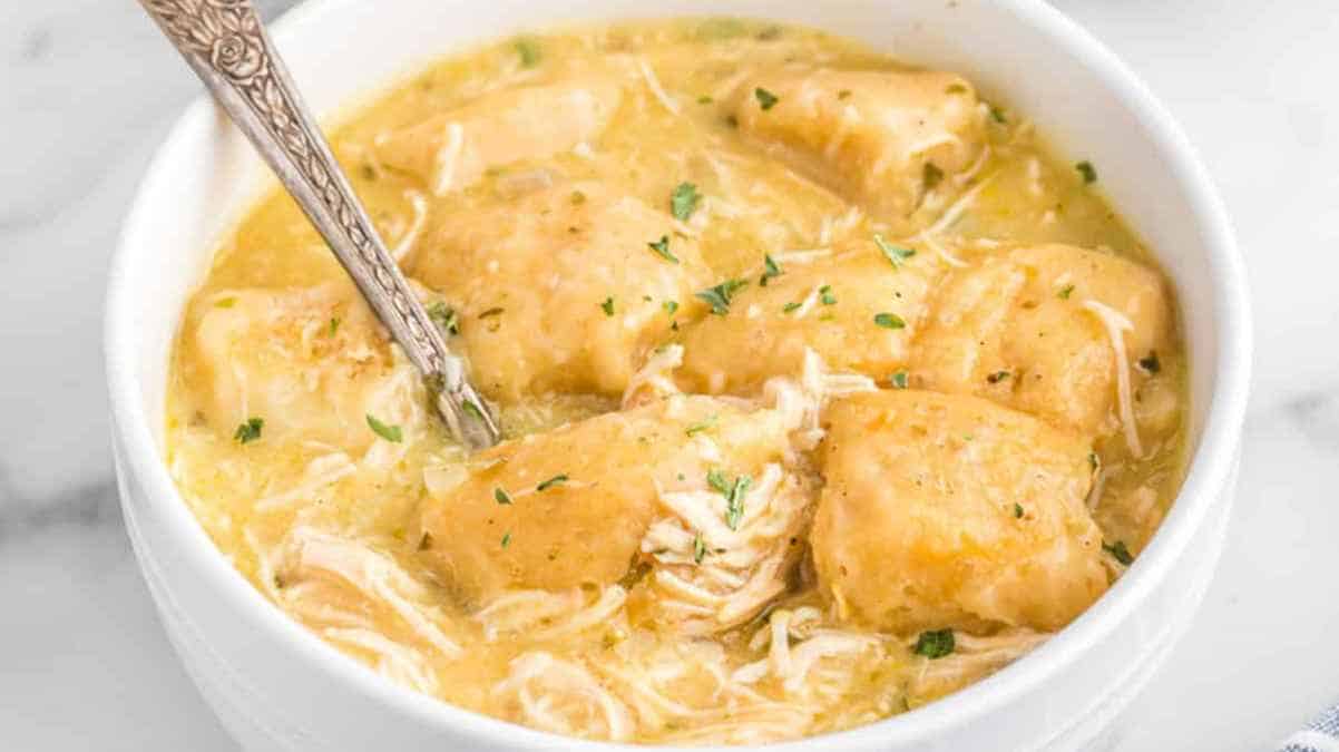 A bowl of chicken and dumplings garnished with herbs.