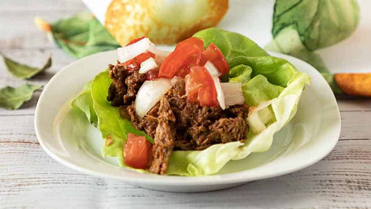 Beef lettuce wrap topped with diced tomatoes and onions on a white plate.