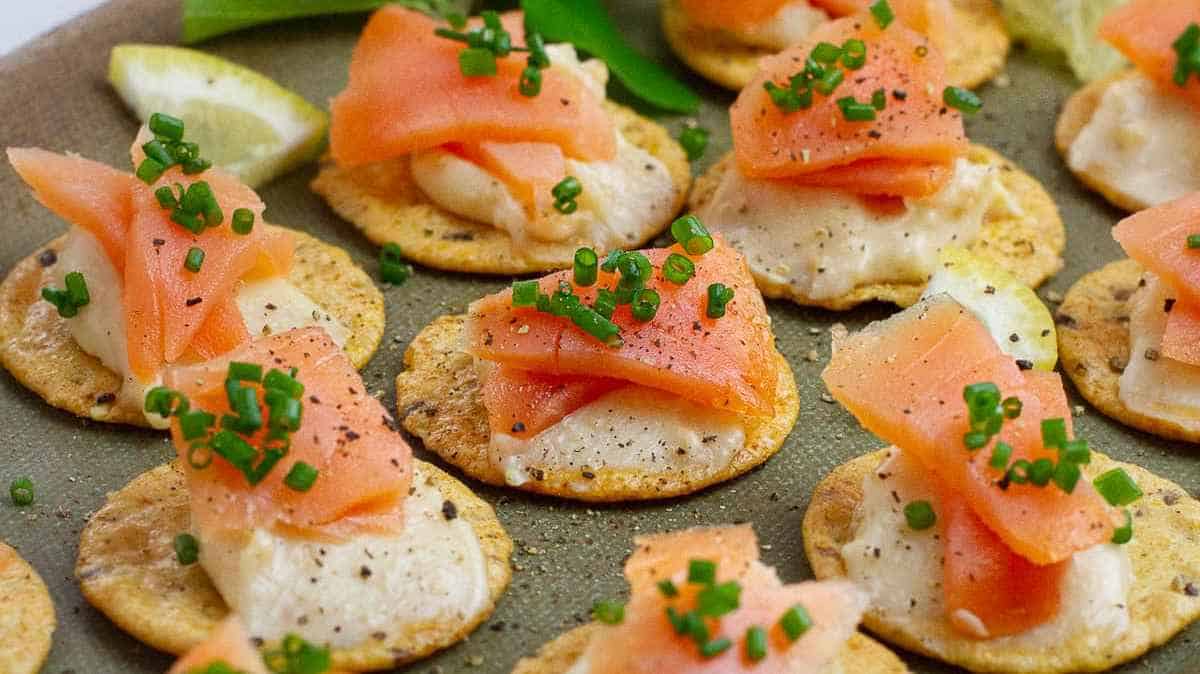 Appetizers with smoked salmon, cream cheese, and chives on crackers.
