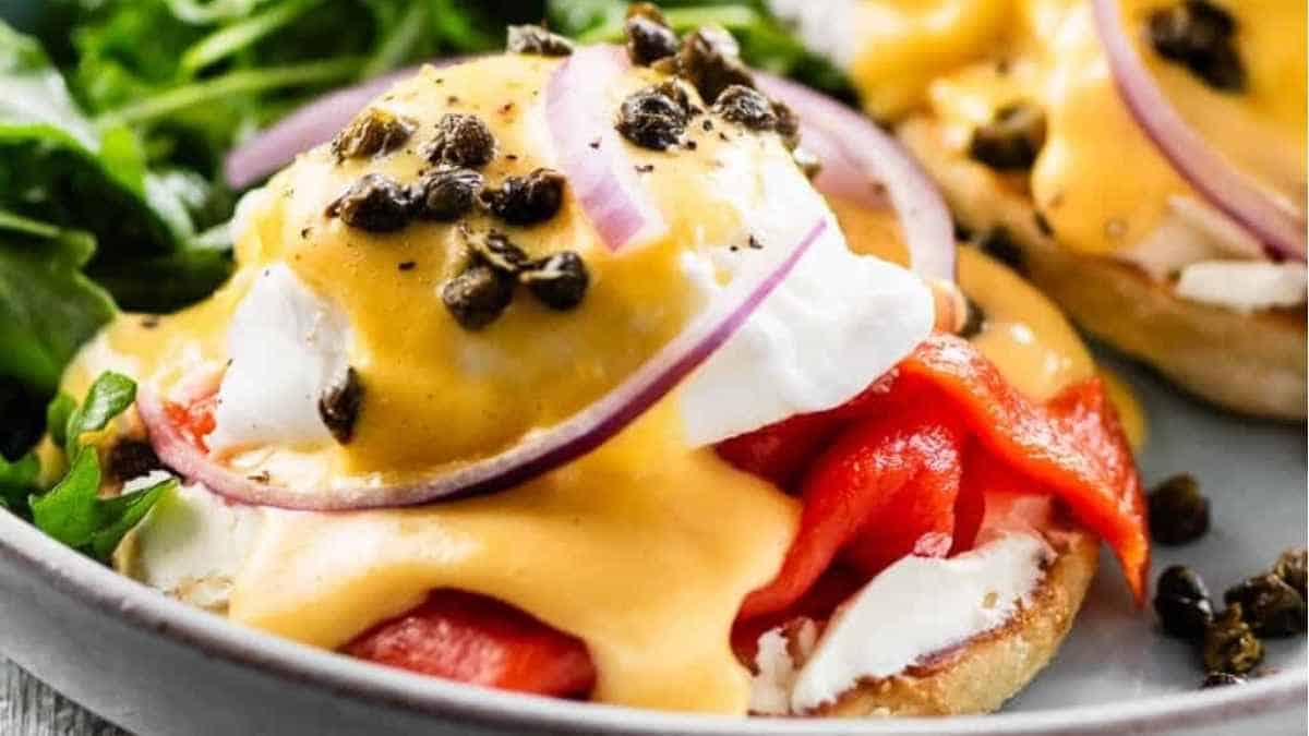 Eggs benedict on a plate with tomatoes and capers.