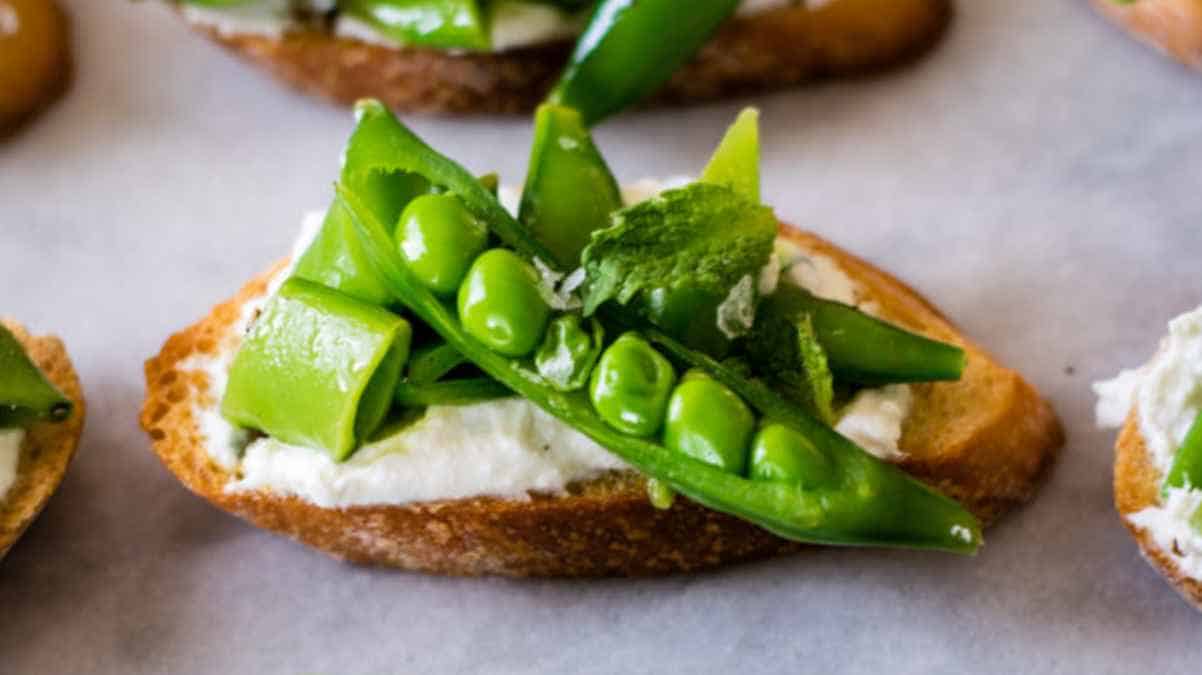 A slice of bread topped with cream cheese, avocado, and green peas on a light-colored background.