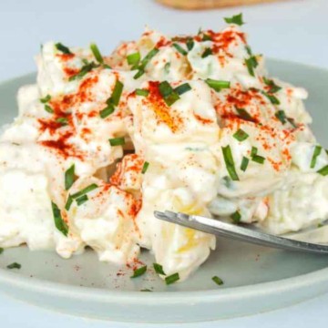 Potato salad garnished with paprika and herbs served on a plate.
