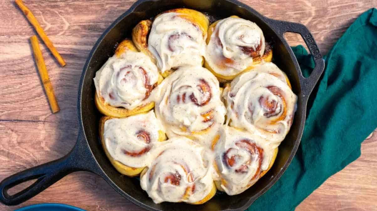 Freshly baked cinnamon rolls with icing in a cast iron skillet.