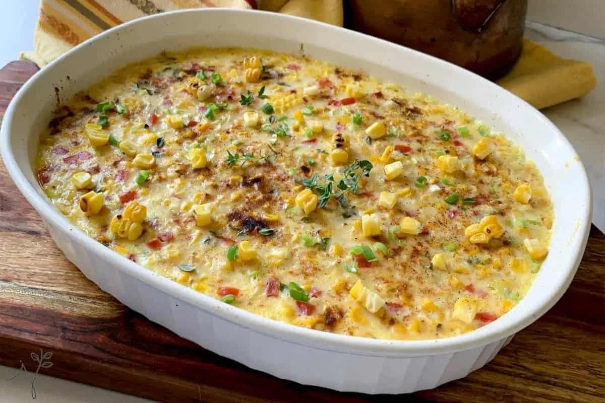 A baked corn casserole in a white dish, garnished with herbs.