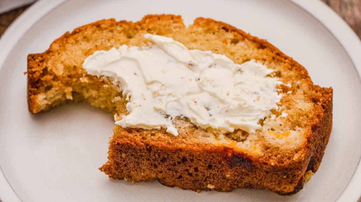 A slice of banana bread with a spread of butter on a plate.