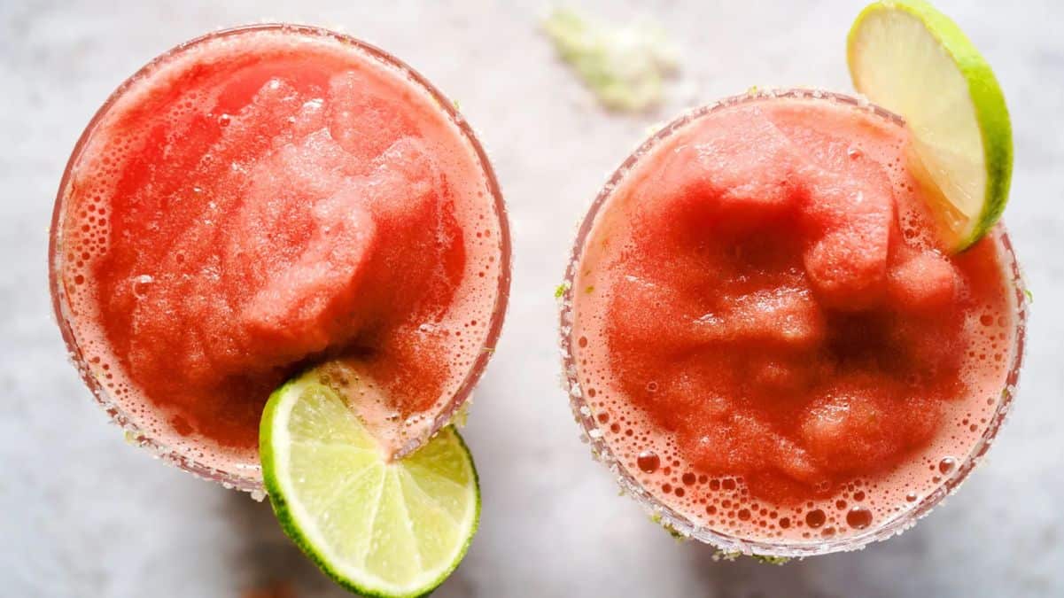 Two strawberry margaritas with salt rims and lime garnishes.