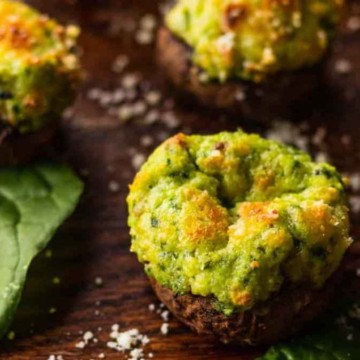 Stuffed mushrooms with a green filling on a wooden surface, garnished with coarse salt and spinach leaves.