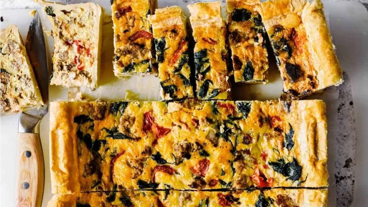 A quiche with spinach and mushrooms on a cutting board.