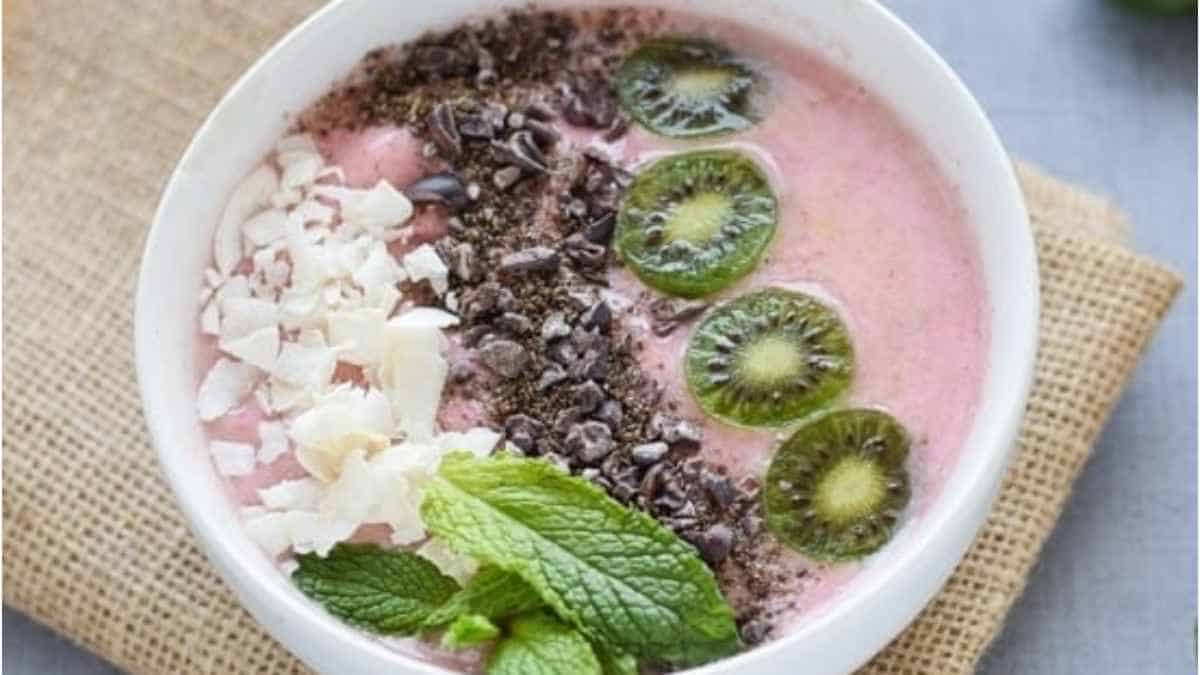A bowl of pink smoothie with kiwi and chocolate chips.