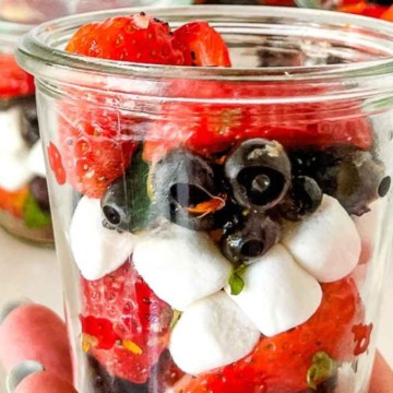 Glass jars filled with layers of strawberries, blueberries, and cream.