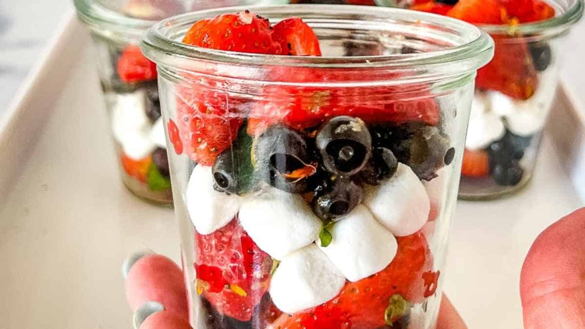 Glass jars filled with layers of strawberries, blueberries, and cream.