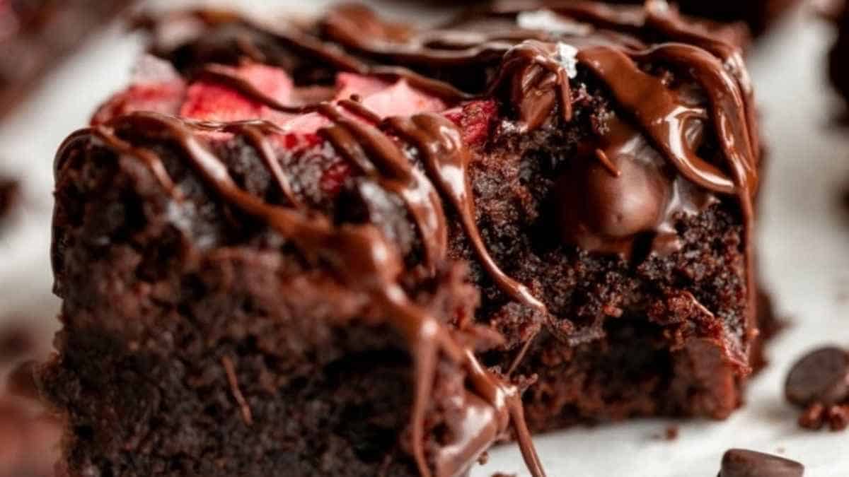 A slice of chocolate brownie with strawberries and chocolate drizzle.