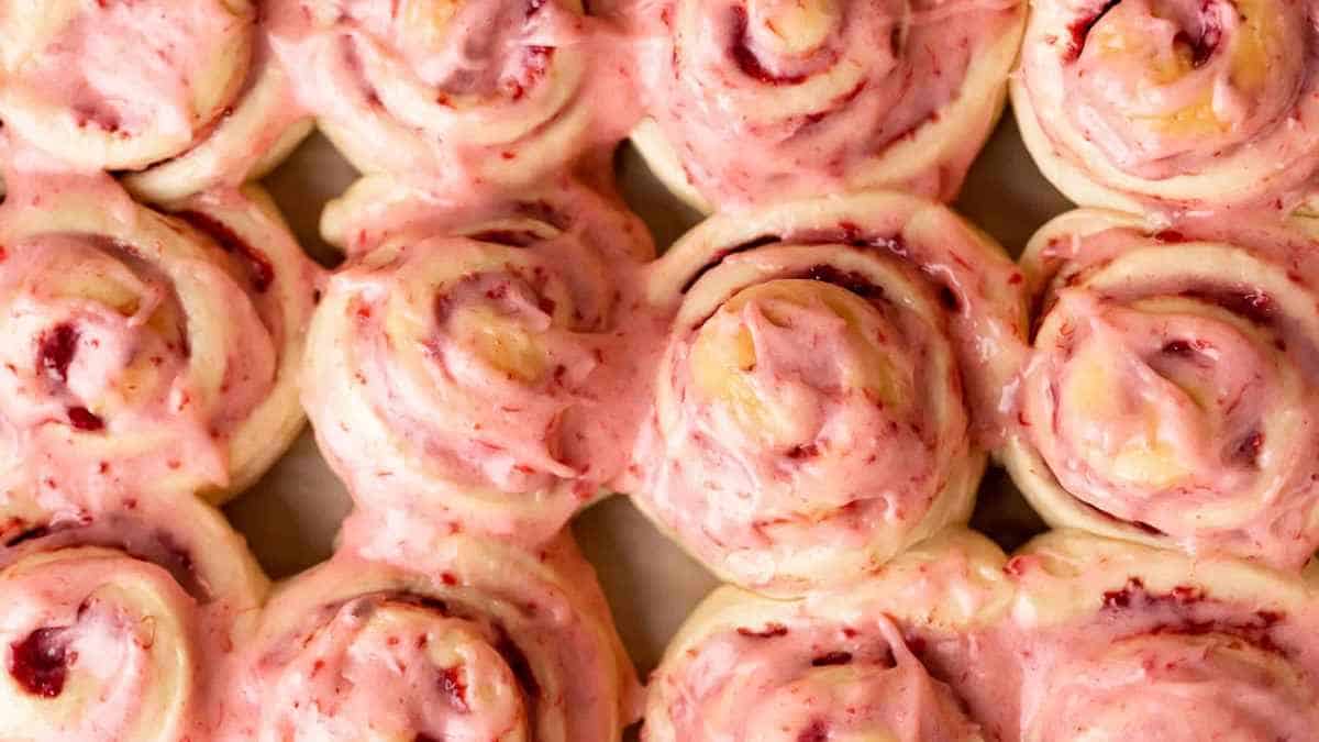 Freshly baked cinnamon rolls with pink icing in a tray.