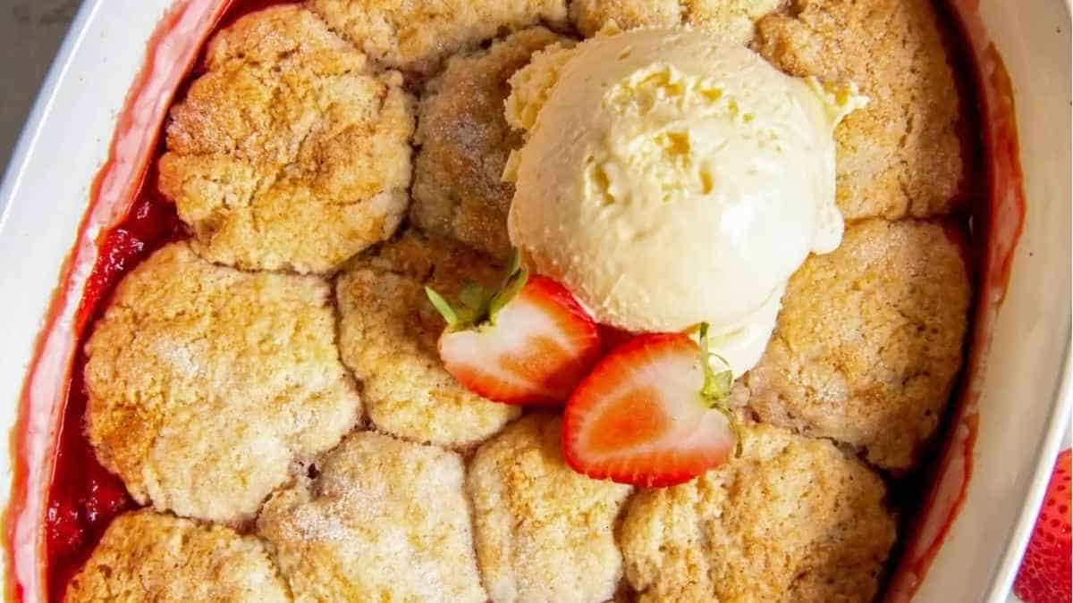 Strawberry cobbler in a white dish with ice cream.