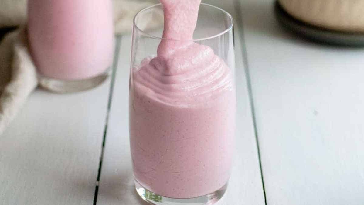 A pink smoothie being poured into a glass.