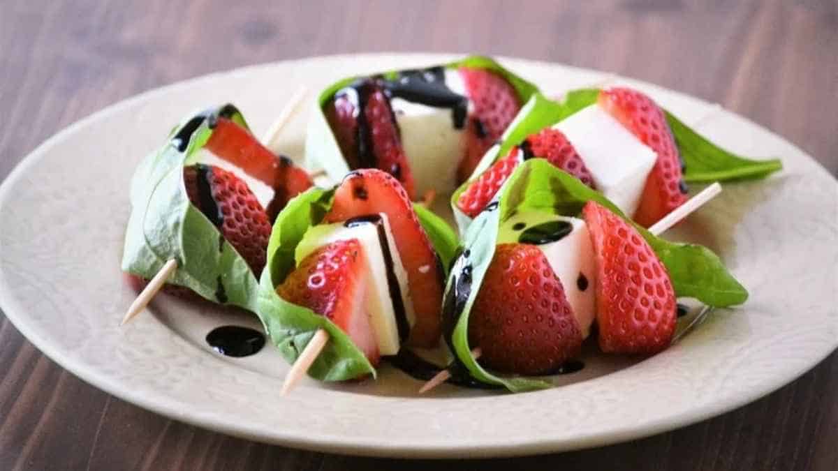 A plate of strawberry and mozzarella salad with basil leaves and balsamic glaze.
