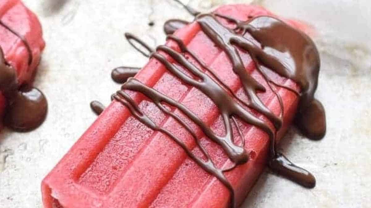 A pink popsicle with chocolate drizzle on it.