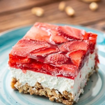 A slice of strawberry cheesecake sits on a blue plate with crumbs and whole strawberries visible in the topping.