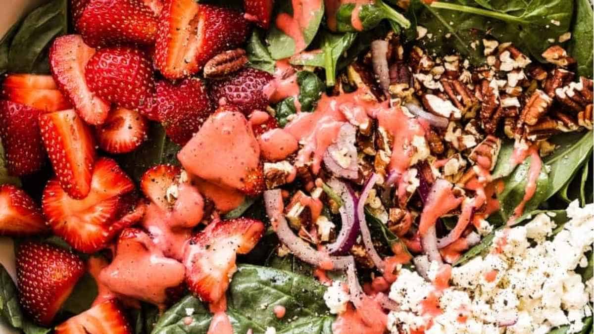A bowl of spinach salad with strawberries and walnuts.
