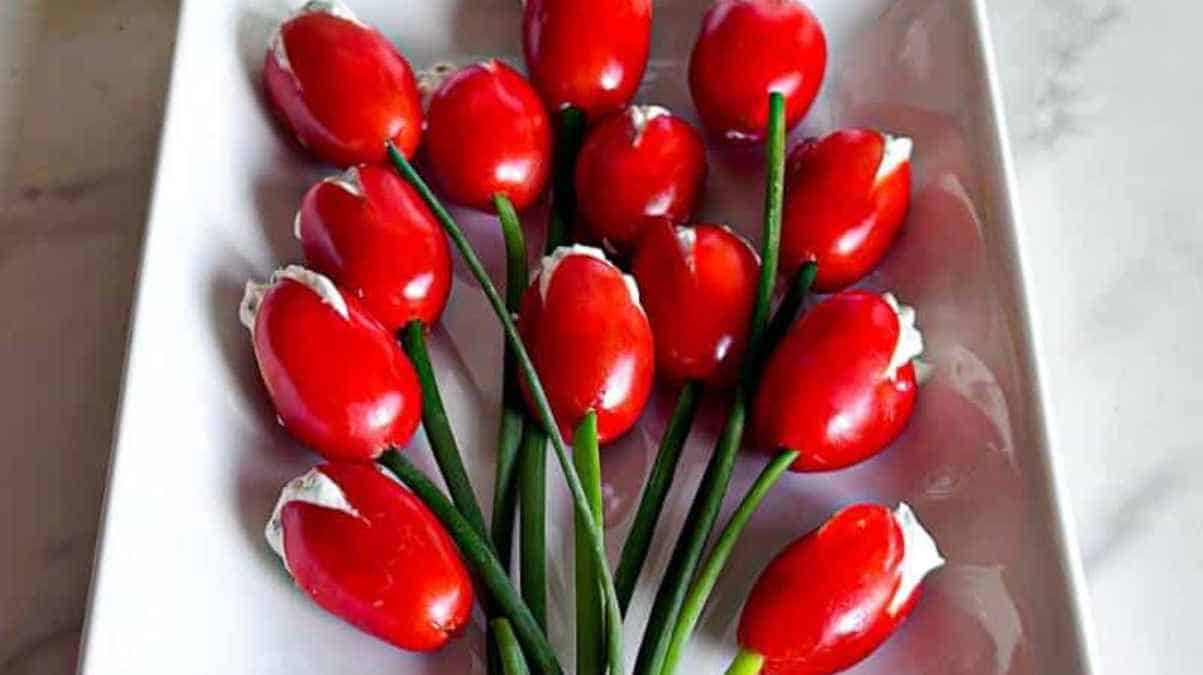 A bouquet of edible tulips made from cherry tomatoes, cream cheese, and chives presented on a white plate.