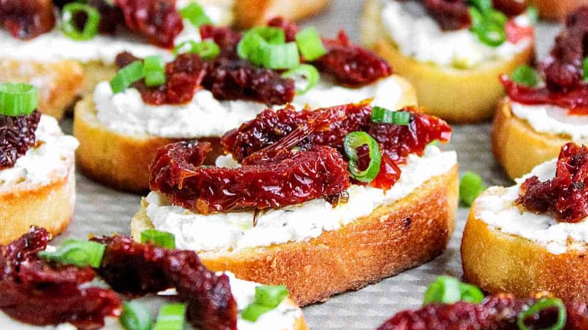 Sliced baguette topped with cream cheese and sun-dried tomatoes, garnished with chopped green onions.