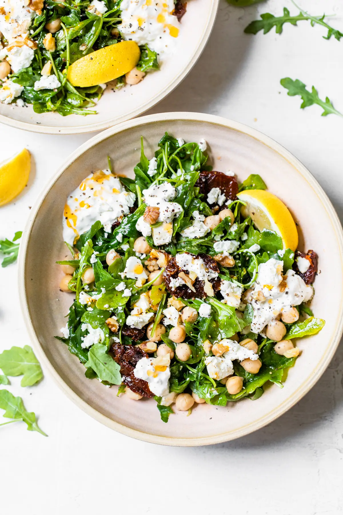 A bowl of salad on a plate, with Sun-dried tomato and Cheese.
