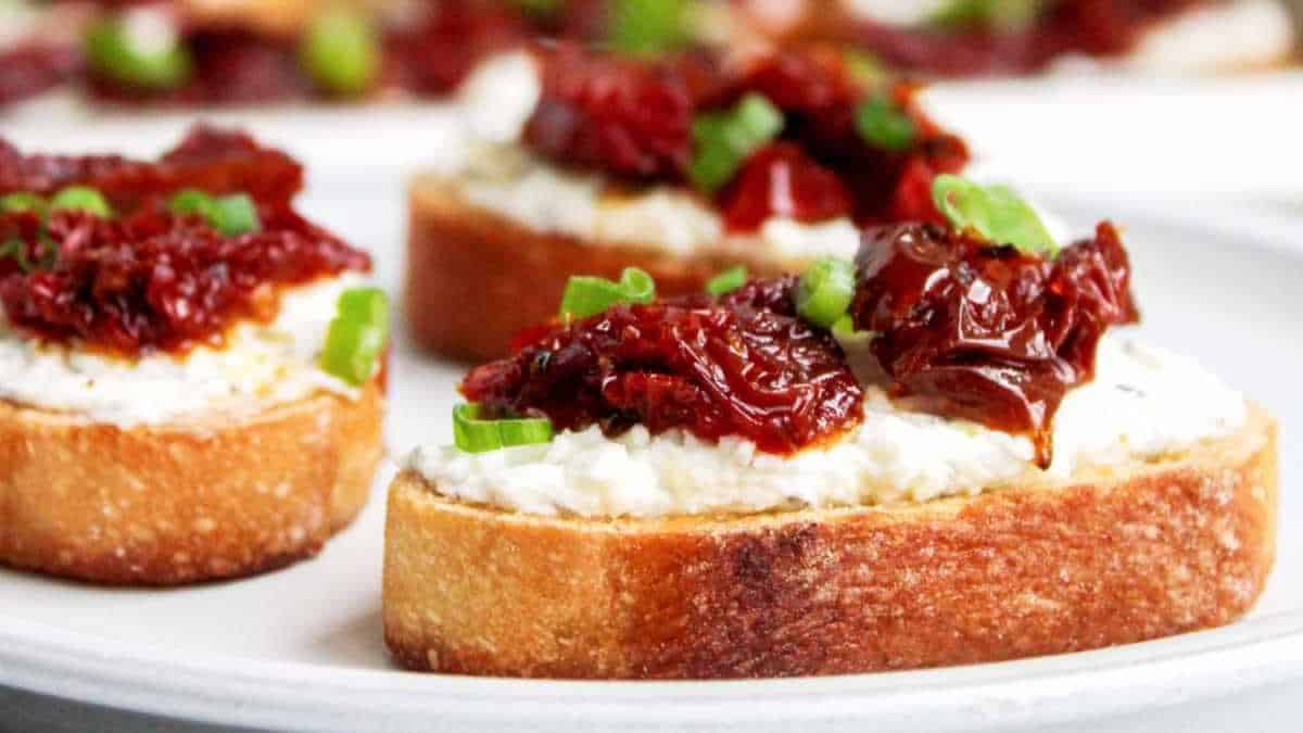 Crostini appetizers with cream cheese and sun-dried tomatoes garnished with chopped green onions.