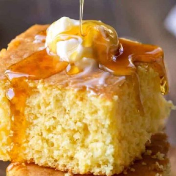 A slice of cornbread topped with melting butter and drizzled with honey.