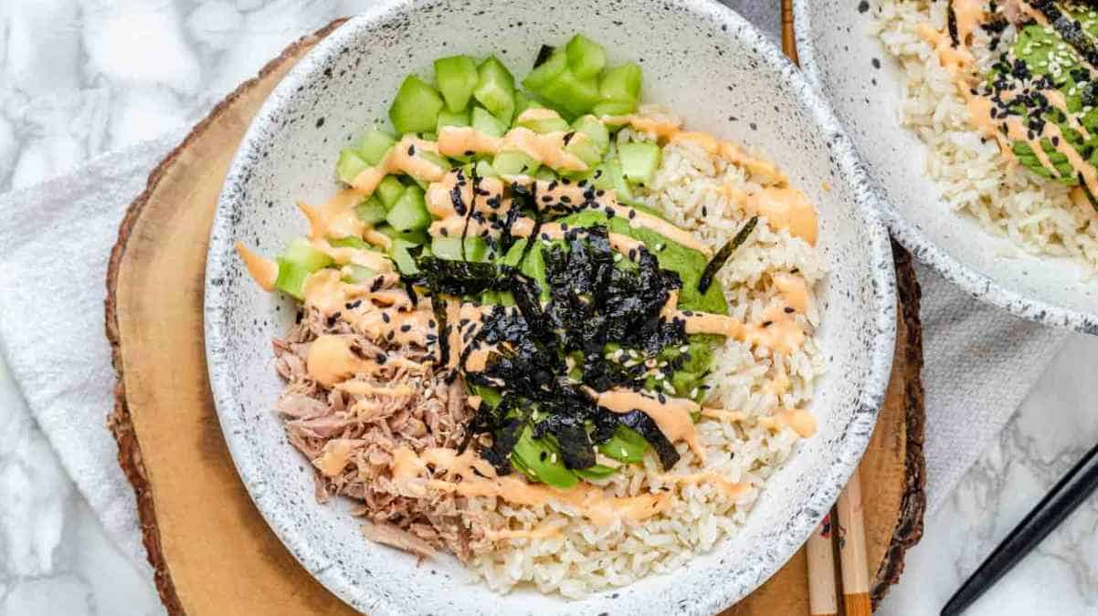 A bowl of rice topped with tuna, cucumber, seaweed, and sesame seeds, served on a wooden platter.