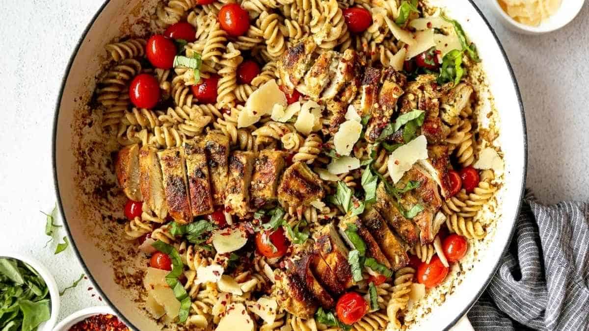 Grilled chicken pasta in a skillet with tomatoes and herbs.