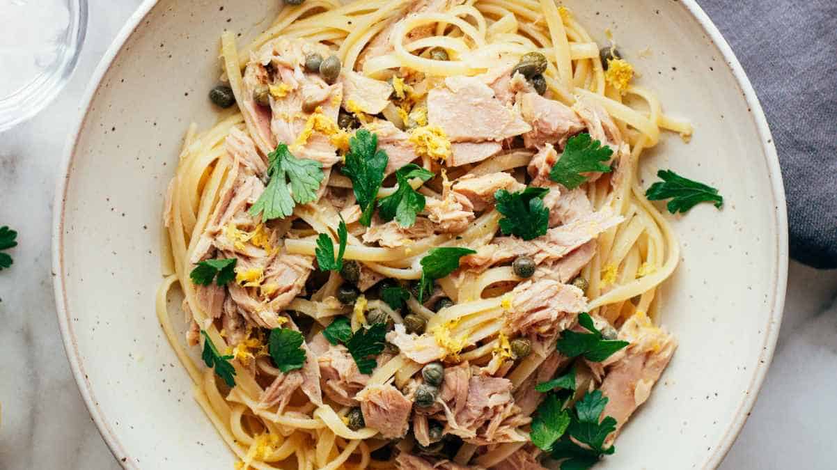 A plate of pasta with flaked tuna, capers, and fresh herbs.
